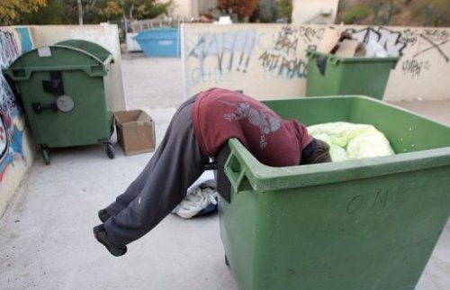 Một người vô gia đang bới rác tìm thức - Ảnh: AFP