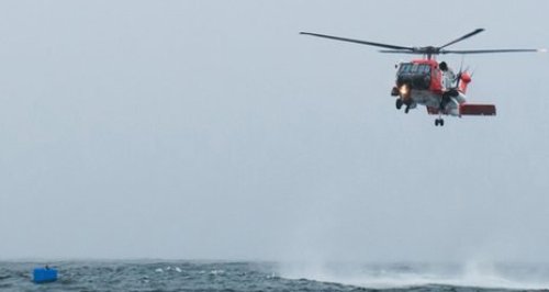 Ảnh chụp lực lượng cứu hộ đáp máy bay đến cứu thủy thủ Harris trên chiếc thùng đựng cá màu xanh (trái) - Ảnh: Reuters
