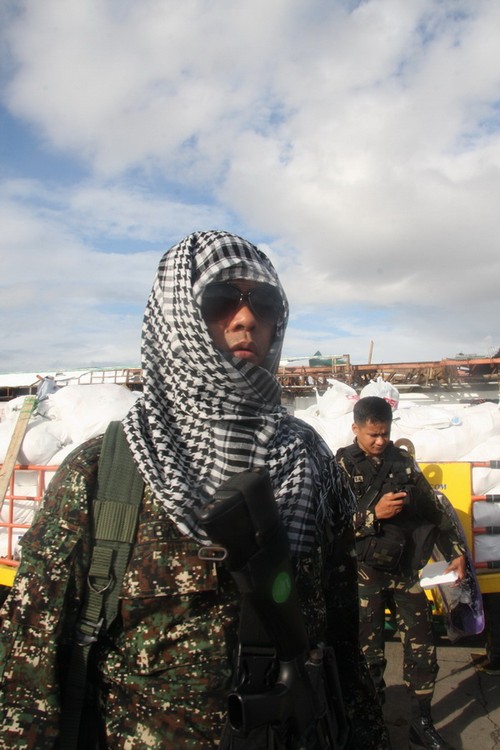 Một binh sĩ Philippines đứng bảo vệ an ninh cho đám đông người di tản đang ngồi bên đường lăn