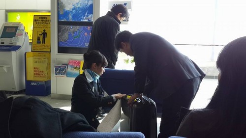 Một nhân viên phục vụ mặt đất của hãng hàng không ANA (Nhật) quỳ gối dưới sàn để giúp khách soạn bớt hành lý trong vali vượt tiêu chuẩn