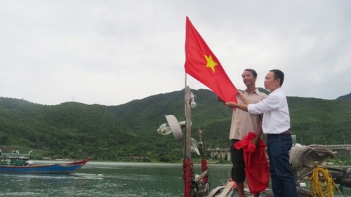 Ngư dân Nguyễn Thế Anh cùng đại diện Báo Thanh Niên treo quốc kỳ mới lên tàu - Ảnh: Tuyết Khoa