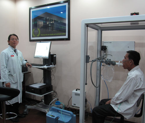 Bệnh nhân Nguyễn Văn T. (bên phải) tái khám sau 6 tuần điều trị, đang được đo phế thân ký buồng kín để kiểm tra các thể tích phổi (ảnh được đăng với sự cho phép của bệnh nhân và gia đình)