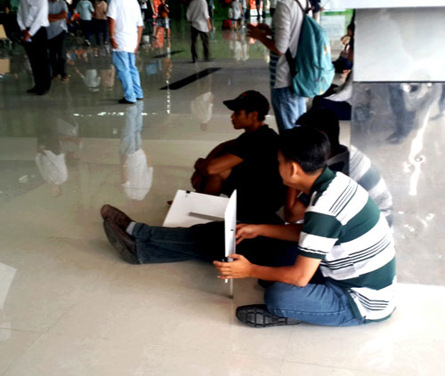 Mõi mòn chờ đợi chuyến bay đến, một số người đón khách ở ga nội địa đã ngồi bệt xuống nhà ga