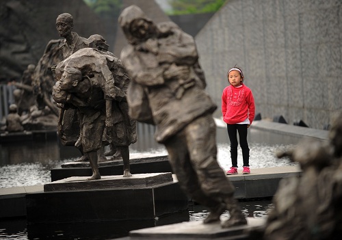 Một bé gái đứng trước các tác phẩm điêu khắc về nạn nhân trong vụ thảm sát Nam Kinh