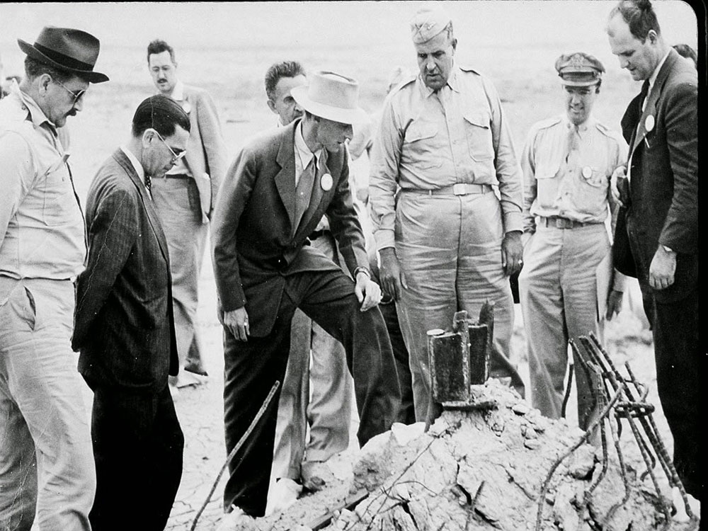 Trưởng Dự án Manhattan, J.Robert Oppenheimer (cúi người) và tướng Leslie Groves (thứ ba, từ phải), người giám sát dự án, đang kiểm tra phần còn lại của vụ nổ nguyên tử đầu tiên - Ảnh: Bộ Năng lượng Mỹ