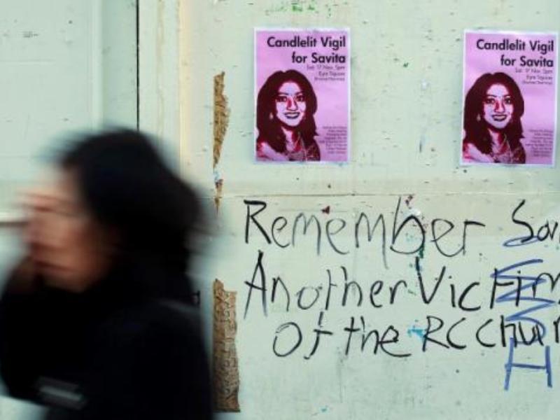 Một người phụ nữ đi ngang qua poster quảng bá về lễ thắp nến cầu nguyện cho người phụ nữ tử vong vì không được phép phá bào thai chết hồi năm 2012 - Ảnh: Reuters