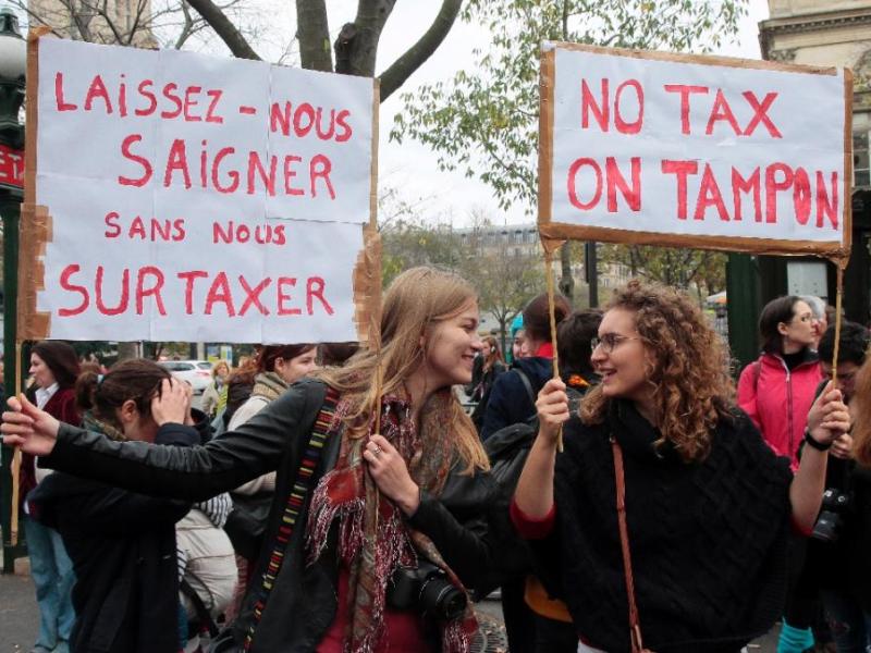 Một phụ nữ cầm biểu ngữ với dòng chữ: “Hãy để chúng tôi chảy máu mà không phải đóng thuế cao” (trái) và “Không đánh thuế tampon” trong cuộc biểu tình ở thủ đô Paris, Pháp ngày 11.11.2015 - Ảnh: AFP
