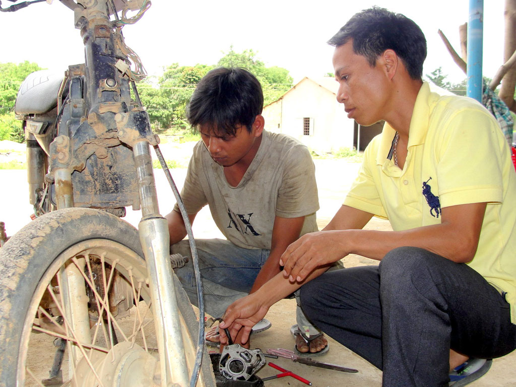 A Thuật (bên phải) hướng dẫn cho thanh niên bản địa học nghề sửa xe máy - Ảnh: Phạm Anh