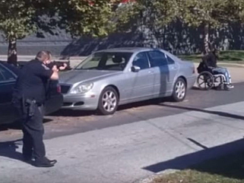Ảnh từ đoạn video cho thấy một sĩ quan cảnh sát Mỹ đang chĩa súng vào người đàn ông người xe lăn – Ảnh màn hình YouTube