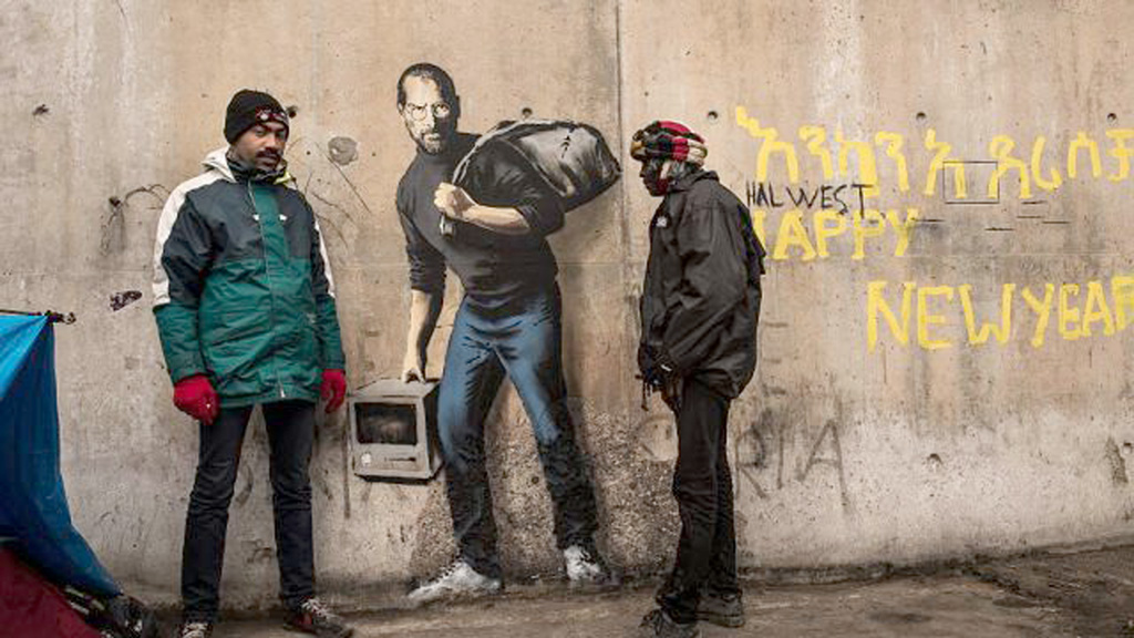 Hai người dân đứng cạnh tác phẩm của họa sĩ đường phố Banksy (Anh) thể hiện Steve Jobs, sáng lập viên tập đoàn Apple trong hình ảnh một người nhập cư từ Syria, ngày 12.12 - Ảnh: AFP