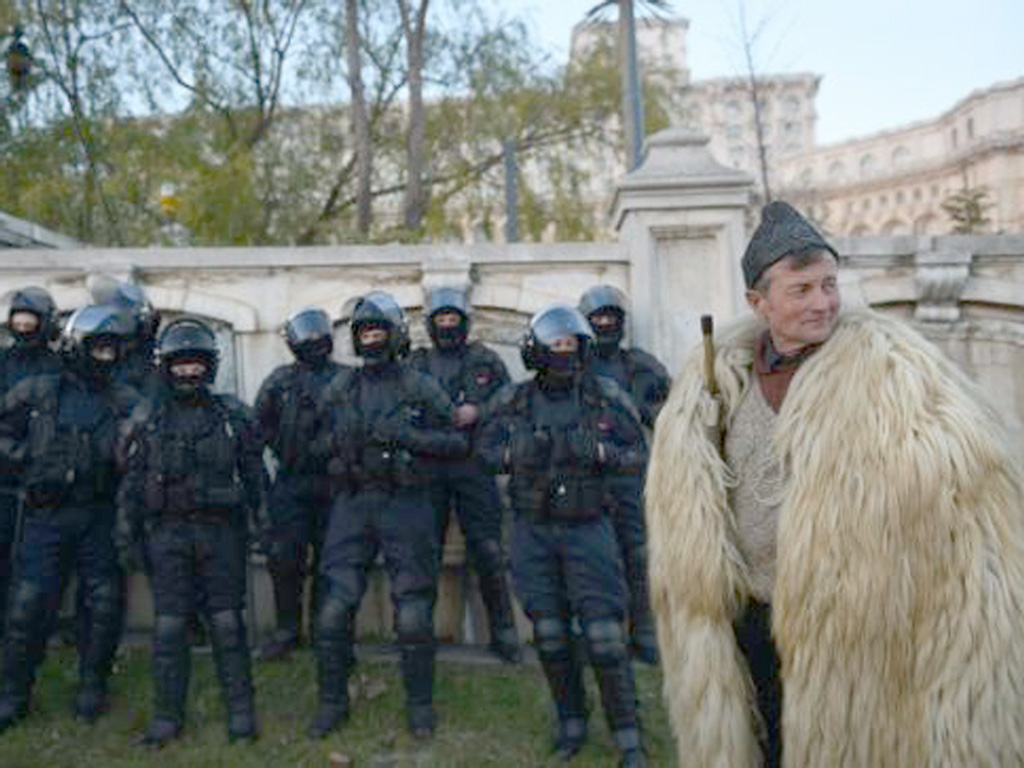 Một nông dân khoác tấm da lông cừu bên cạnh hàng rào cảnh sát trước tòa nhà Quốc hội Romania ngày 15.12 - Ảnh: AFP