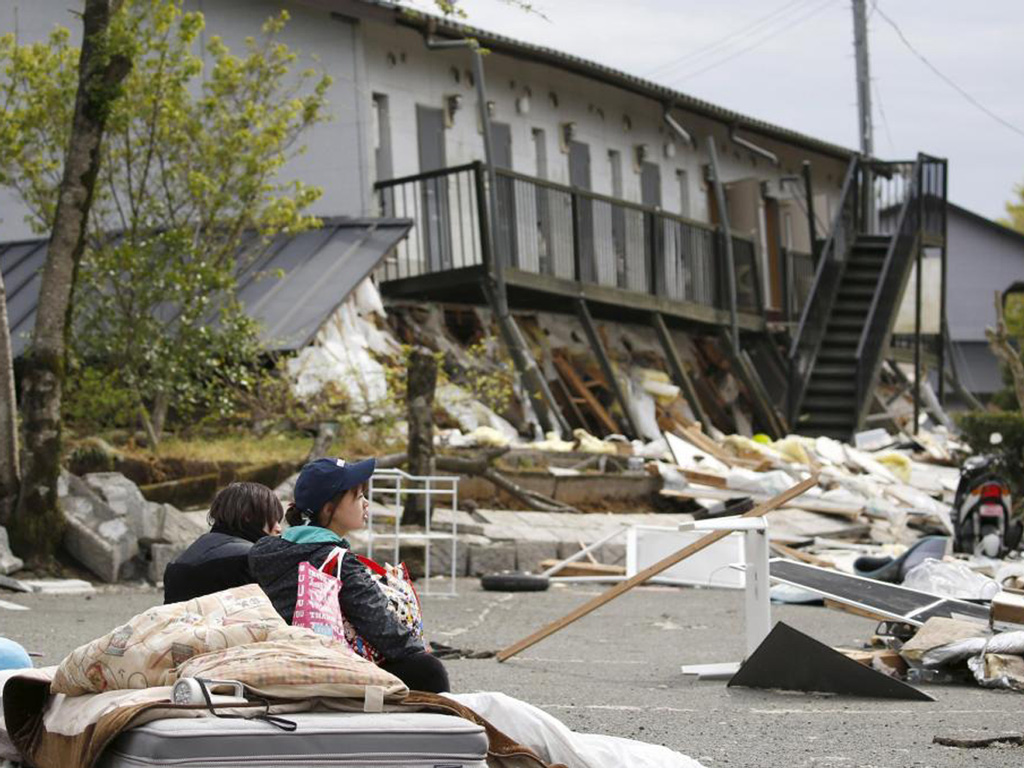 Hai sinh viên đại học ngồi nghỉ trước khu ký túc xá bị sập một phần do động đất tại thị trấn Minamiaso, tỉnh  Kumamoto (phía nam Nhật Bản) ngày 16.4 - Ảnh: Reuters