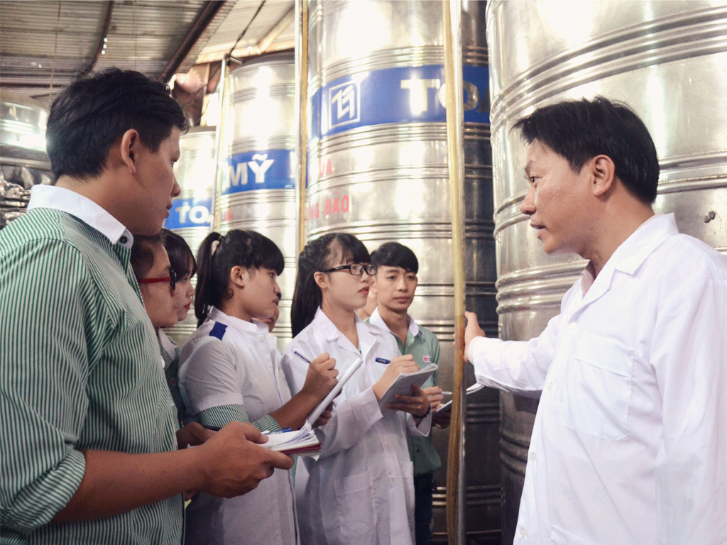 Đại diện doanh nghiệp hướng dẫn SV khoa Công nghệ thực phẩm xem thể tích rượu trong bồn chứa - xưởng thực hành Công ty Minh Anh
