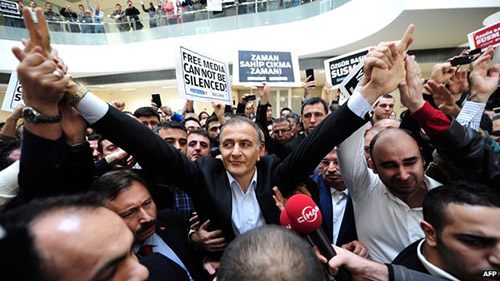 Tổng biên tập tờ Zaman Ekrem Dumanli giơ tay đáp lại nhân viên của mình khi bị cảnh sát áp giải 