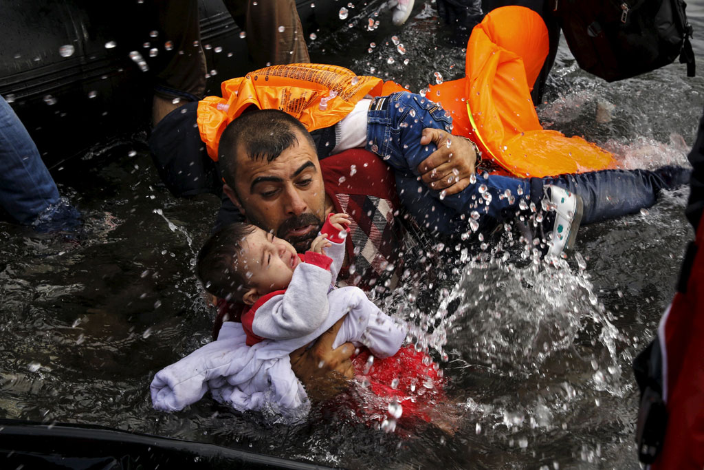 Một người tị nạn Syria ôm chặt hai con khi cố gắng rời khỏi chiếc xuồng tới đảo Lesbos của Hy Lạp vào ngày 24.9.2015. Họ đã vượt hành trình dài từ Thổ Nhĩ Kỳ đến Hy Lạp qua biển Aegea - Ảnh: Reuters