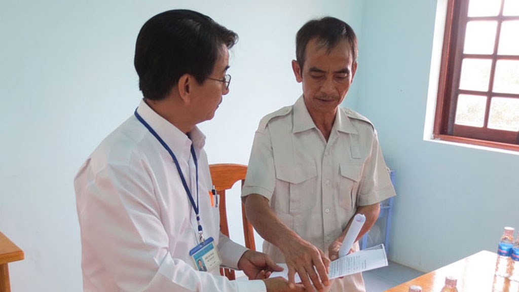 Phó Chánh án TAND tỉnh Bình Thuận Hoan hướng dẫn ông Nén làm giấy yêu cầu bồi thường oan sai - Ảnh: Quế Hà