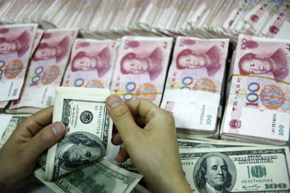Đồng đô la Mỹ đang được đếm cạnh các cọc tiền mệnh giá 100 nhân dân tệ - Ảnh: AFP