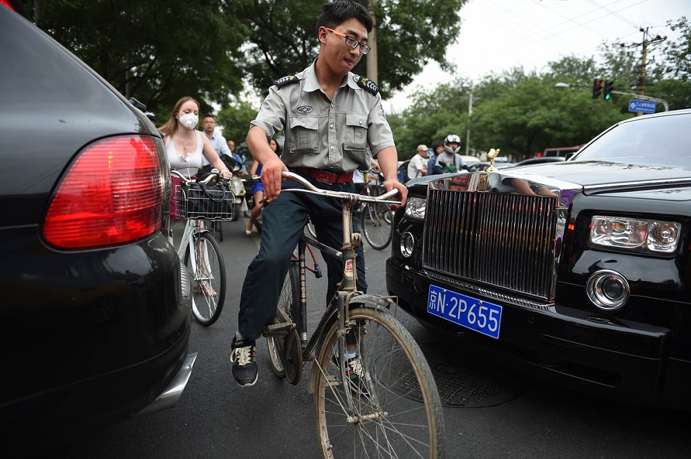 Một người đàn ông đi xe đạp lách giữa hai chiếc Rolls-Royce và Porsche trên đường phố Bắc Kinh - Ảnh: AFP