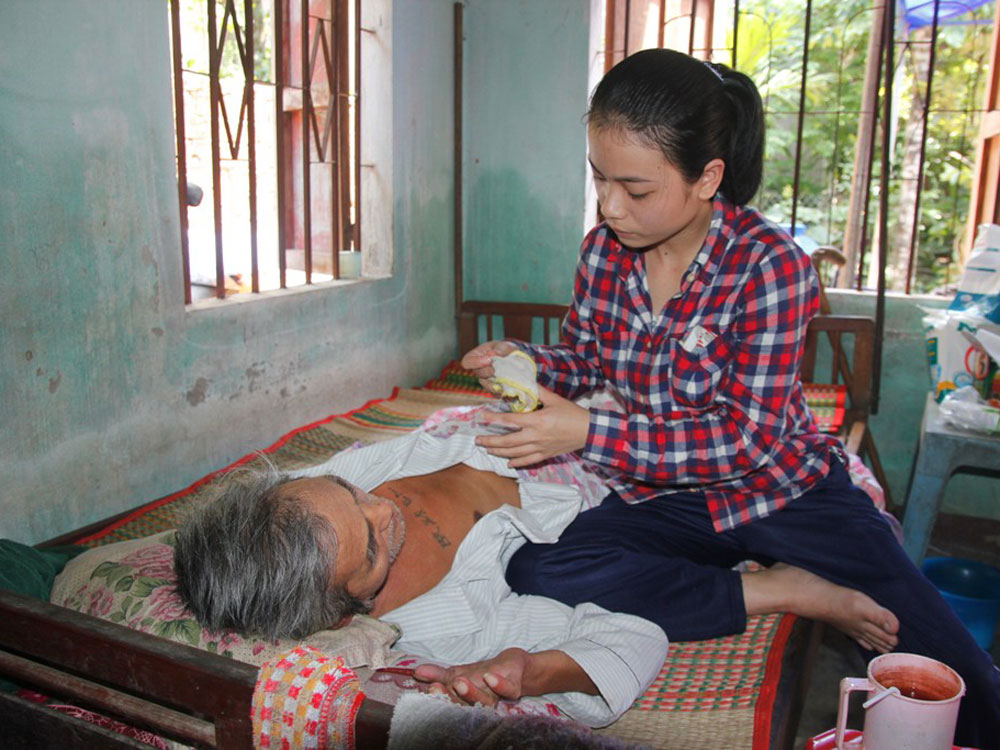 Nguyễn Thị Quang Nhi chăm sóc cho người cha đang nằm liệt giường - Ảnh: Hoàng Sơn