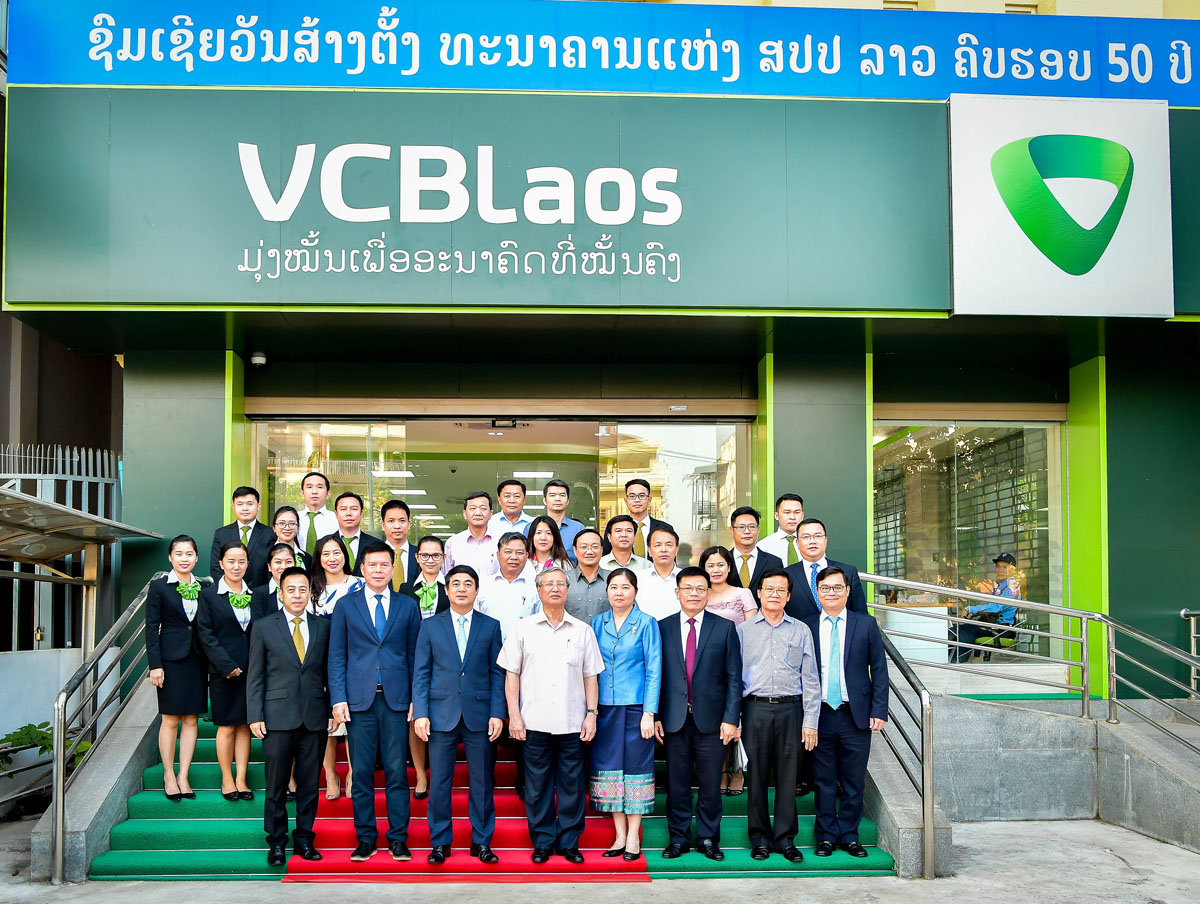 Đồng chí Trần Quốc Vượng, Ủy viên Bộ Chính trị, Thường trực Ban Bí thư Trung ương Đảng CSVN (thứ 4 từ trái sang, hàng thứ nhất) chụp hình lưu niệm với Đại diện Ban lãnh đạo Vietcombank, Ban giám đốc và cán bộ nhân viên Vietcombank Lào trước Trụ sở Vietcombank Lào tại Viên Chăn