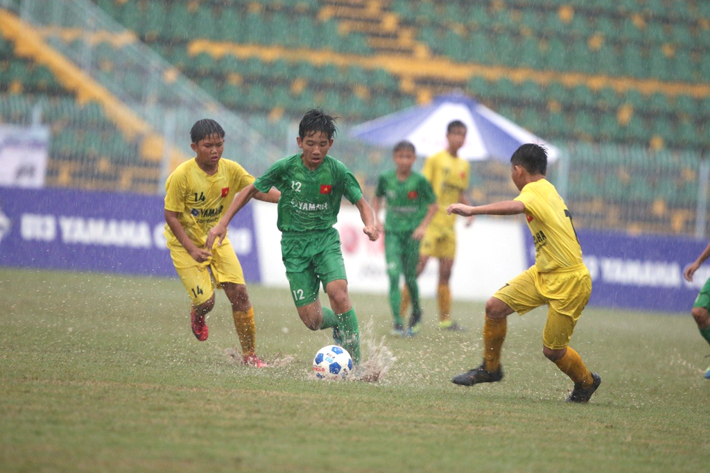 Cơn mưa lớn kéo dài khiến các cầu thủ U13 Phú Nhuận (áo vàng) và U13 Đắk Lắk (áo xanh) phải thay đổi chiến thuật liên tục để giành lấy cơ hội ghi bàn