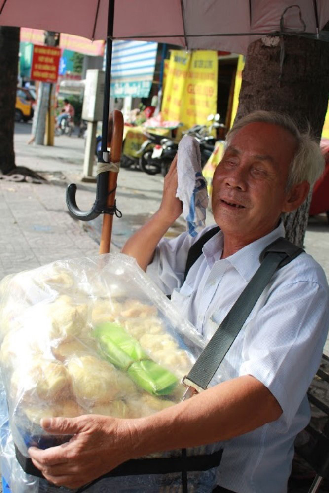 Dù hai mắt không nhìn thấy gì nhưng hơn 20 năm qua ông Quang vẫn ngồi trên vỉa hè bán bánh nuôi vợ.