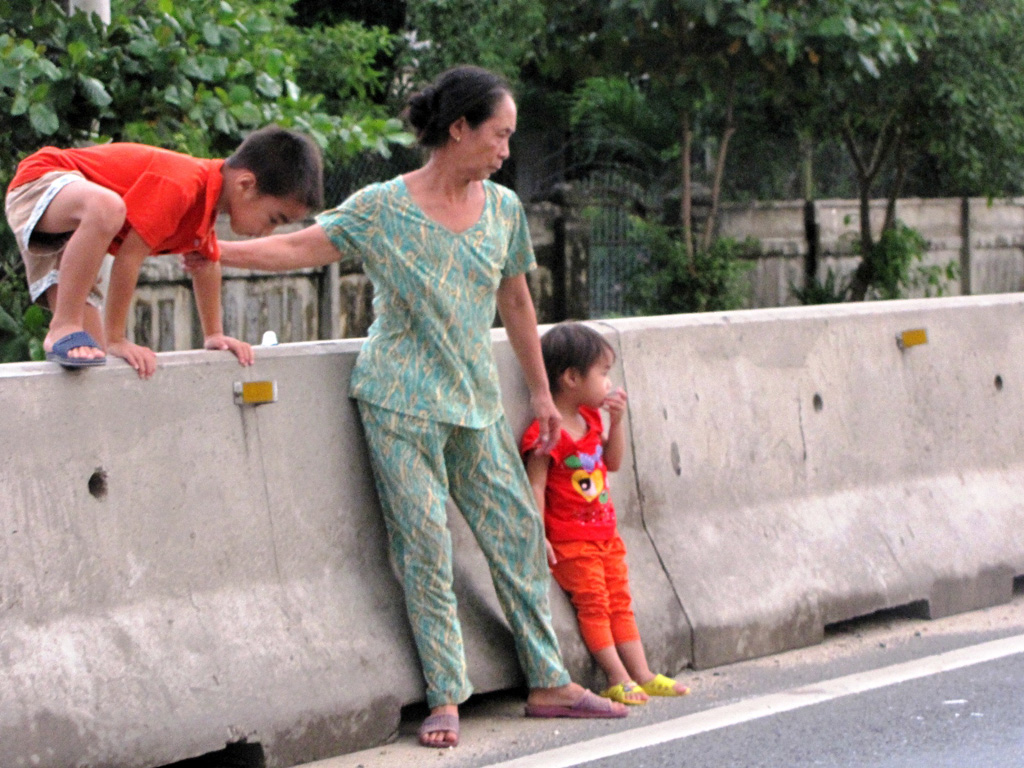 Người lớn vô ý dẫn trẻ em leo qua dải phân cách, em bé trong ảnh sợ khép nép khi xe ô tô liên tục lao qua