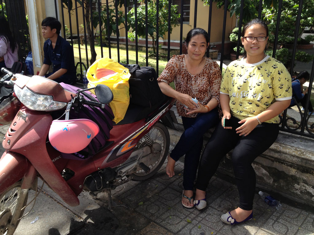 Chị Phan Đặng Cẩm Tiên, “Cô hàng xóm tốt bụng”, ngồi đợi bên ngoài, mắt luôn dõi về trường thi trong lúc thí sinh Nguyễn Thị Hồng Nho đang trong phòng thi.