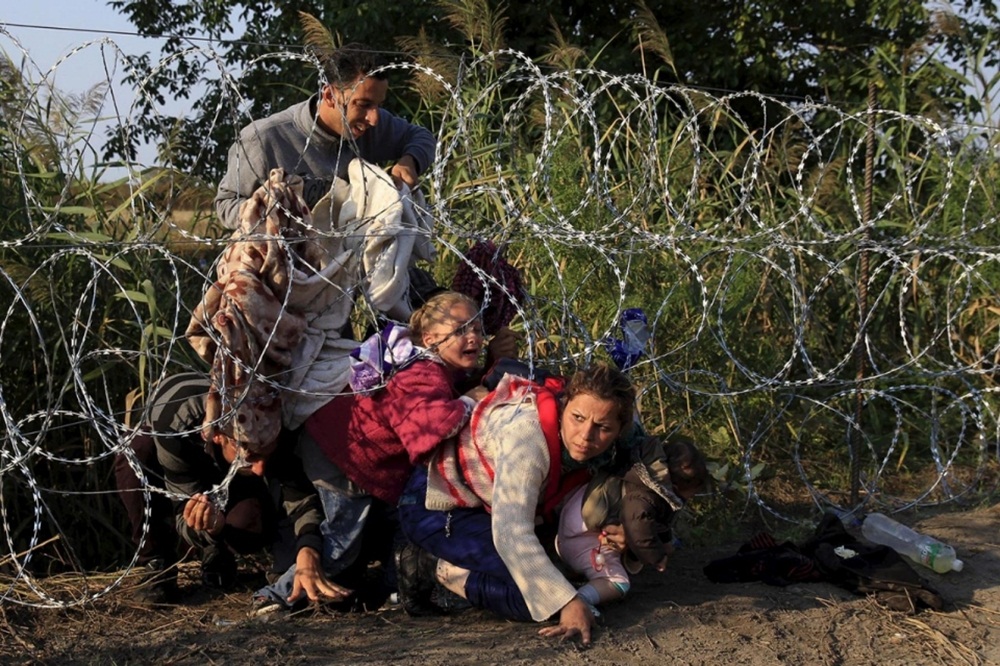 Người tị nạn cố vượt qua hàng rào kẽm gai dọc biên giới Hungary - Ảnh: Reuters