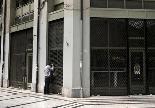 Một người đàn ông nhìn vào khu cửa hàng đã đóng cửa ở trung tâm Athens - Ảnh: Reuters
